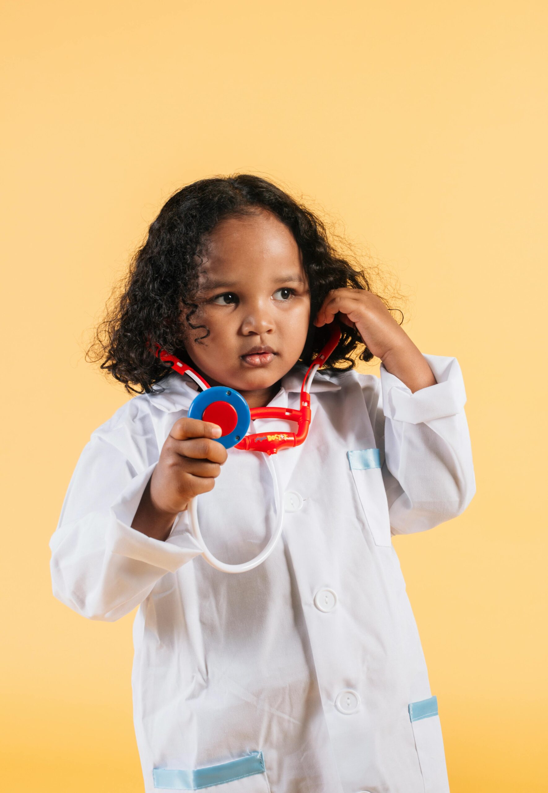 Cute child dressed as a doctor with a stethoscope against a yellow background.